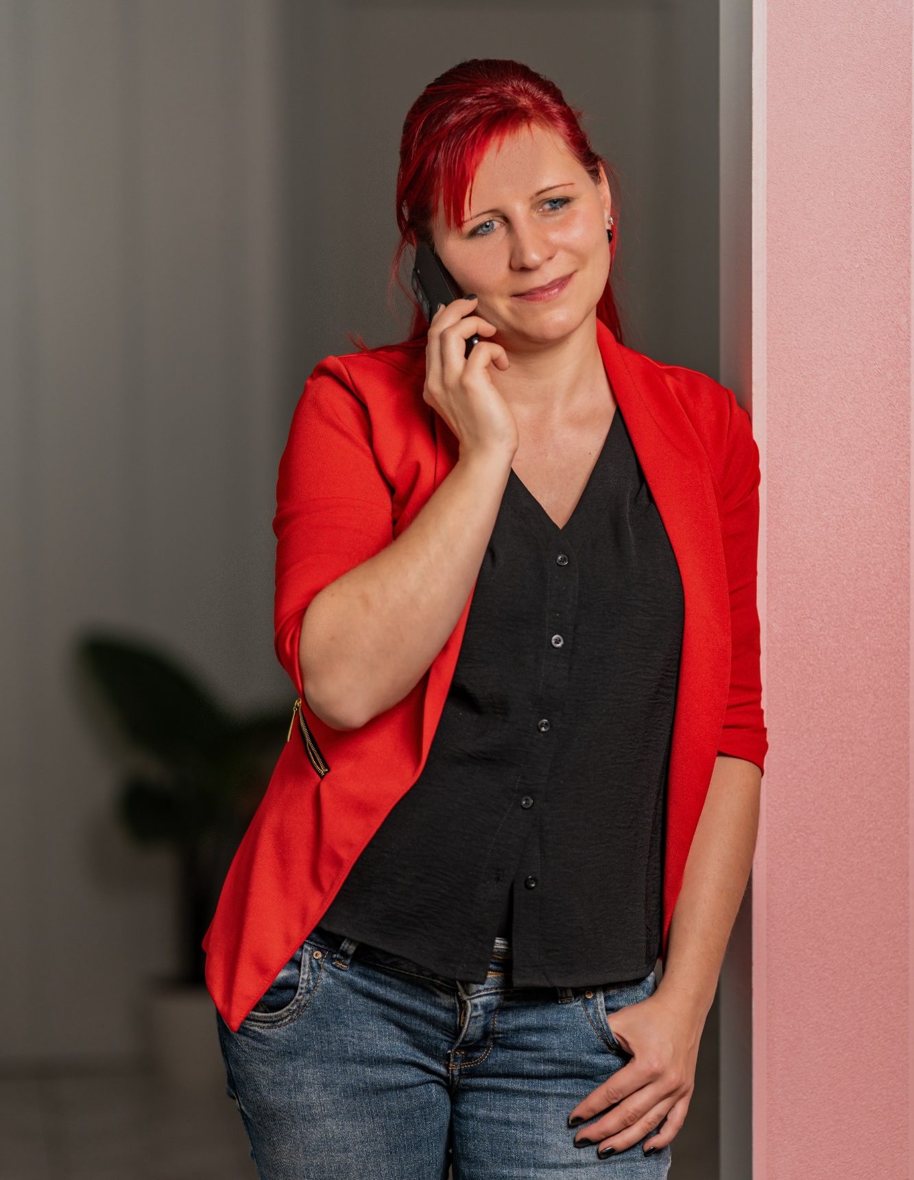 Frau mit rotem Blazer und schwarzem Oberteil, die am Telefon lächelt.