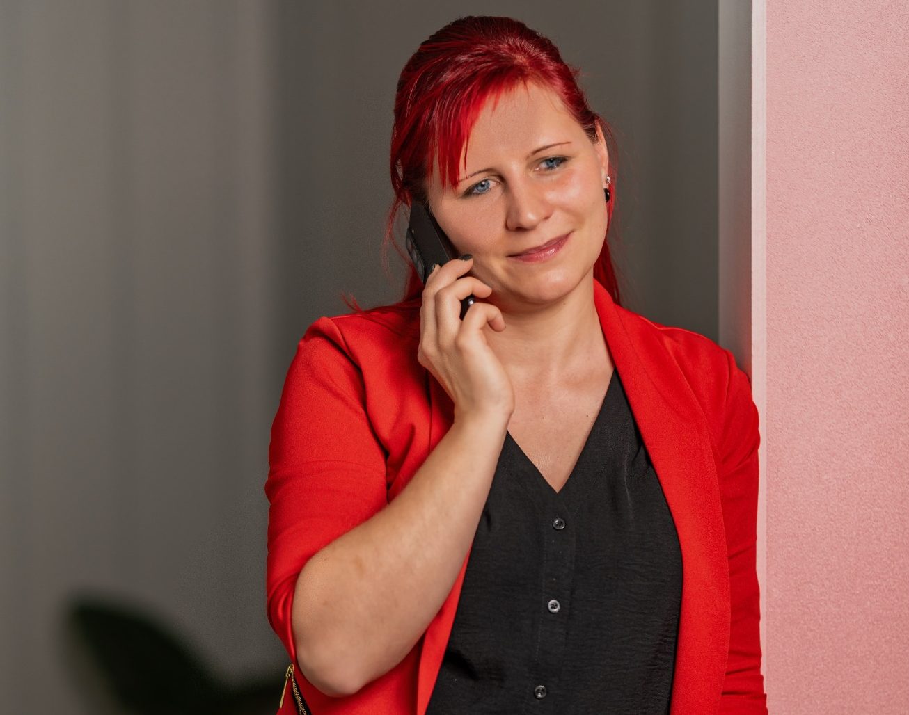 Frau mit roten Haaren und rotem Blazer, die ein Tablet in der Hand hält.