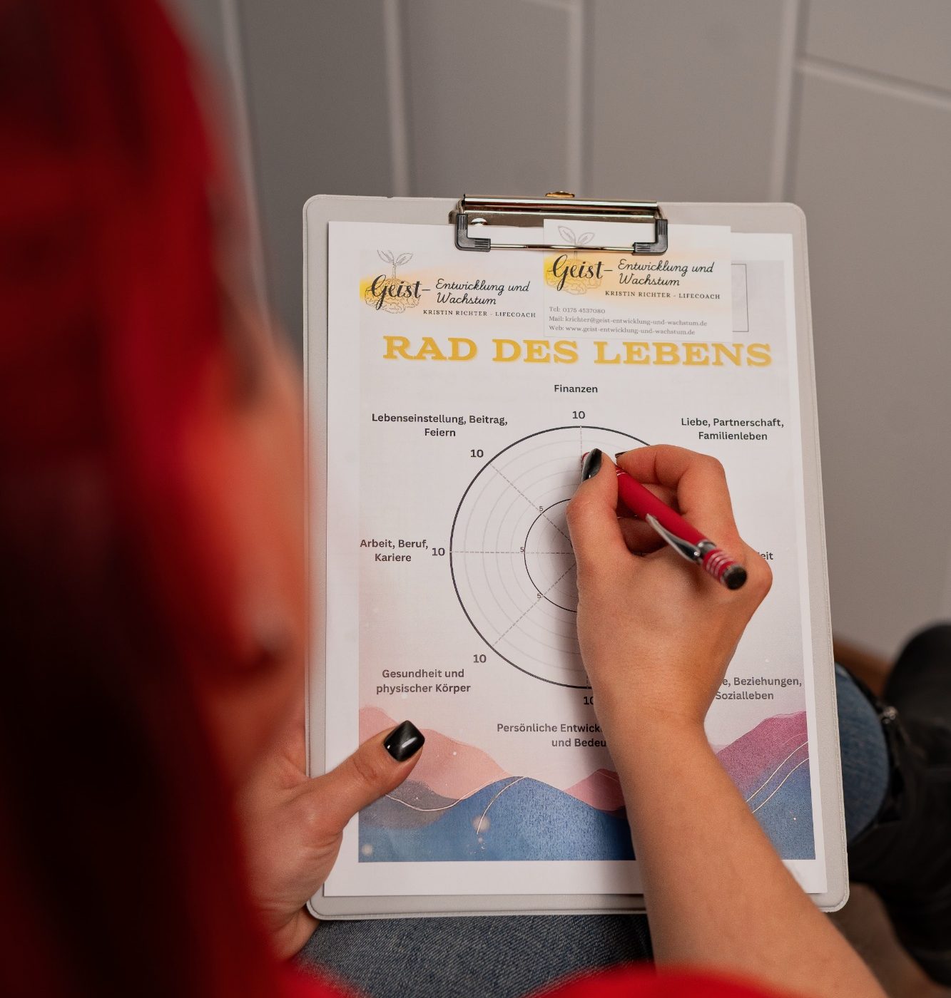 Eine Hand mit pinkem Stift schreibt auf ein Arbeitsblatt mit Diagramm und Text.